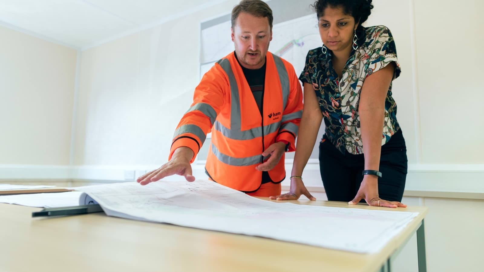 Two engineers reviewing project blueprints in an office, discussing details