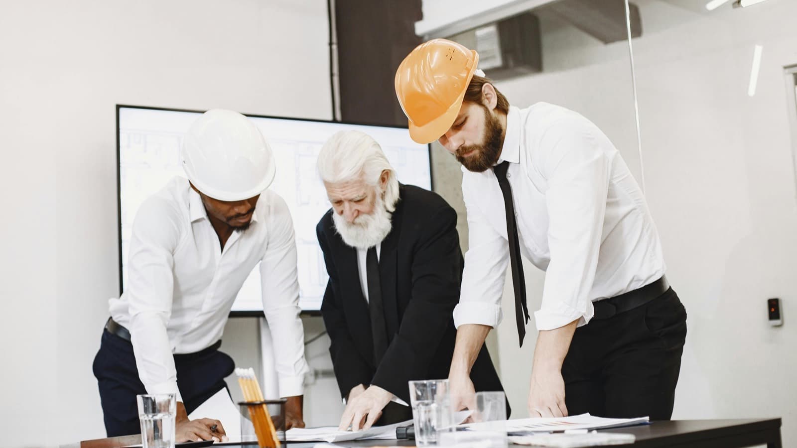 Group of professional engineers in hardhats reviewing project blueprints in a modern office